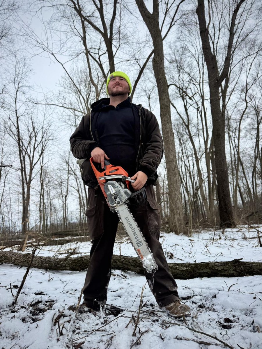 Brady Vail, founder of Vail Wood Products, in the woods with a chainsaw in Butler, Indiana